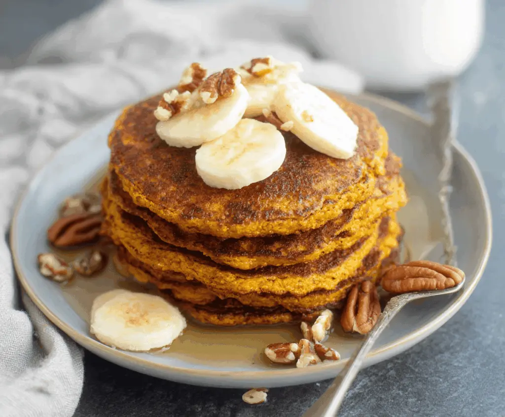 Creamy blender pumpkin oatmeal pancakes topped with fresh fruit and maple syrup on a plate