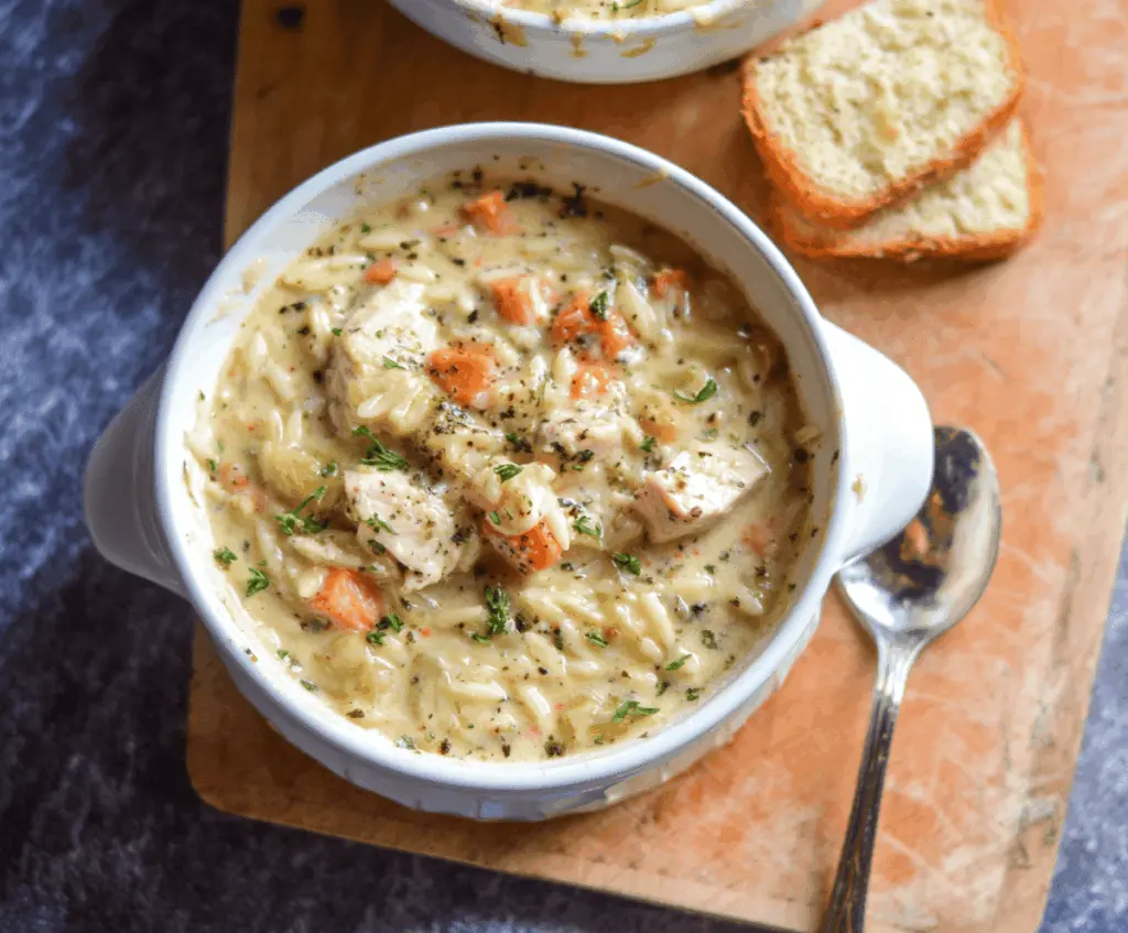 A bowl of creamy chicken orzo soup garnished with fresh herbs, showcasing tender chicken, orzo pasta, and vegetables in a rich, velvety broth.