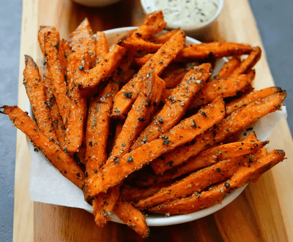Golden garlic sweet potato fries served with fresh herbs on a rustic plate, perfect for a healthy snack or side dish.