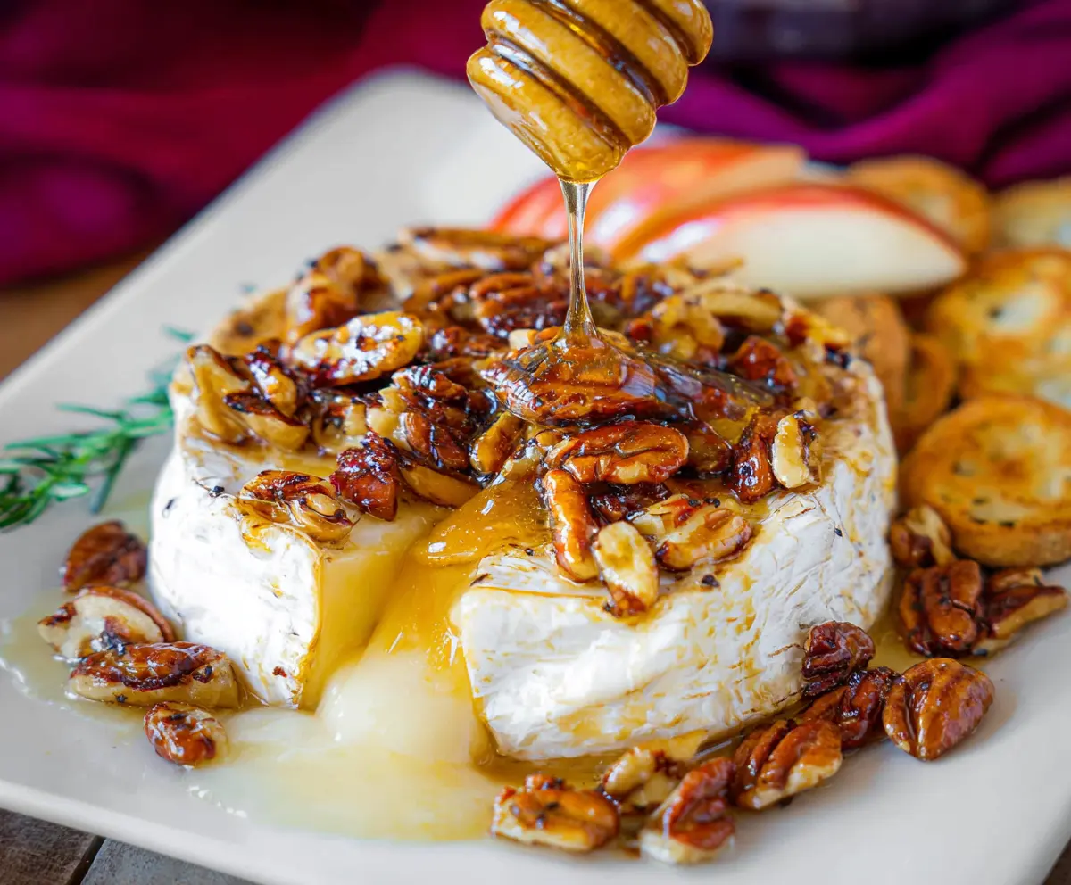 Delicious baked brie cheese topped with honey and mixed nuts, served as a gourmet appetizer.