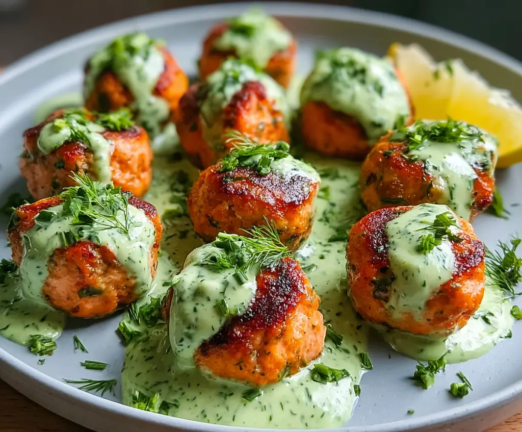 Delicious baked salmon meatballs served with a vibrant tangy avocado sauce on a white plate.