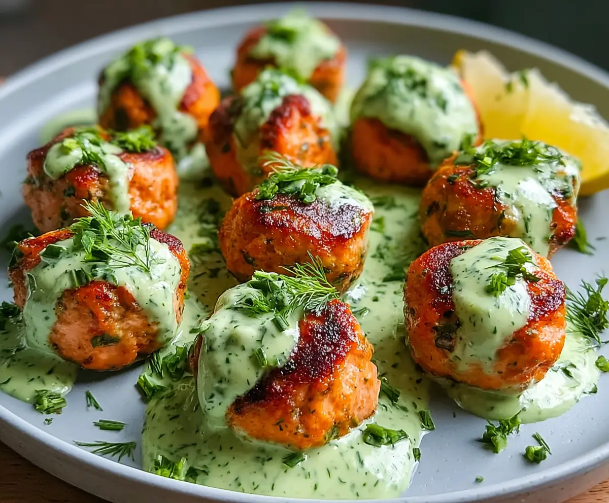 Delicious baked salmon meatballs served with a vibrant tangy avocado sauce on a white plate.