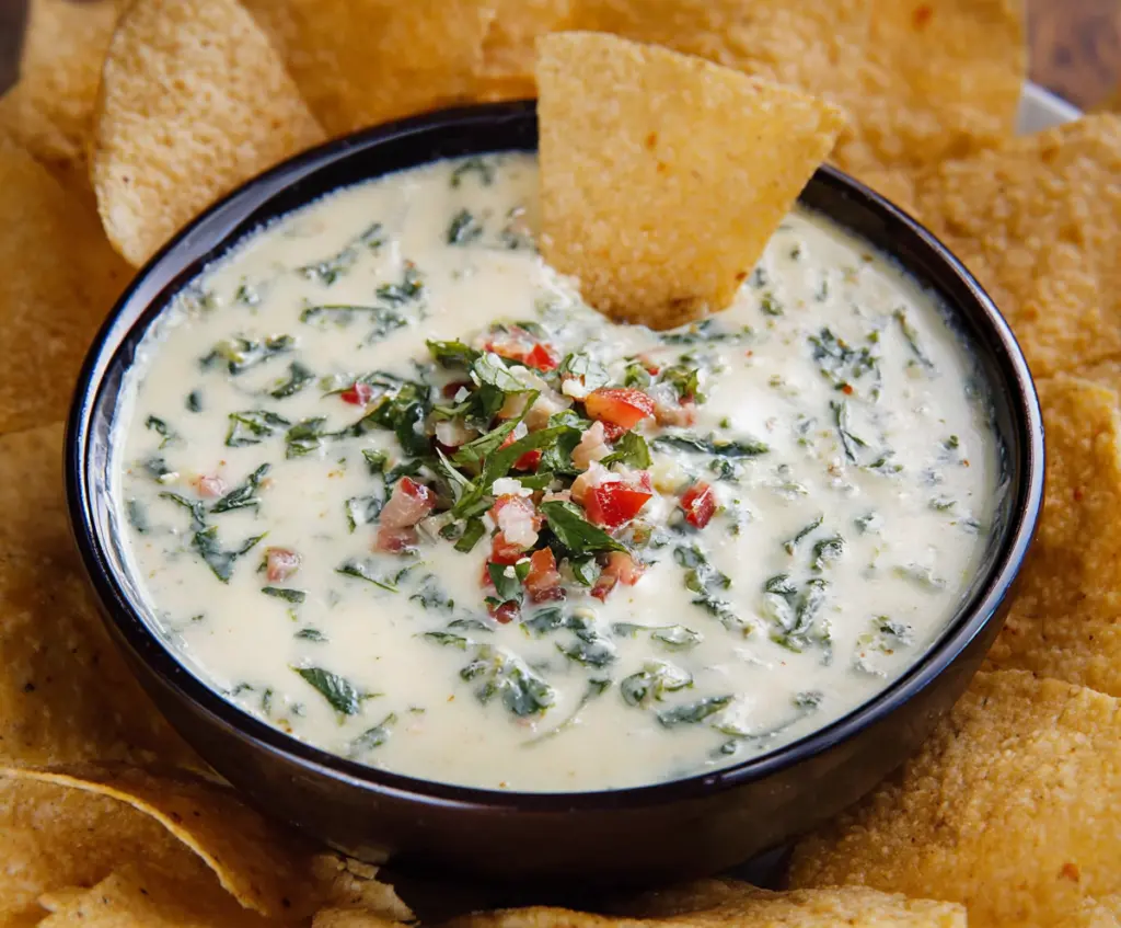 Creamy White Spinach Queso served in a bowl with crispy tortilla chips on the side.