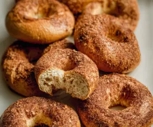Freshly baked cinnamon bagels with a glossy crust on a wooden surface.