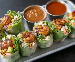 Delicious blackened shrimp spring rolls with fresh vegetables and herbs on a white plate.