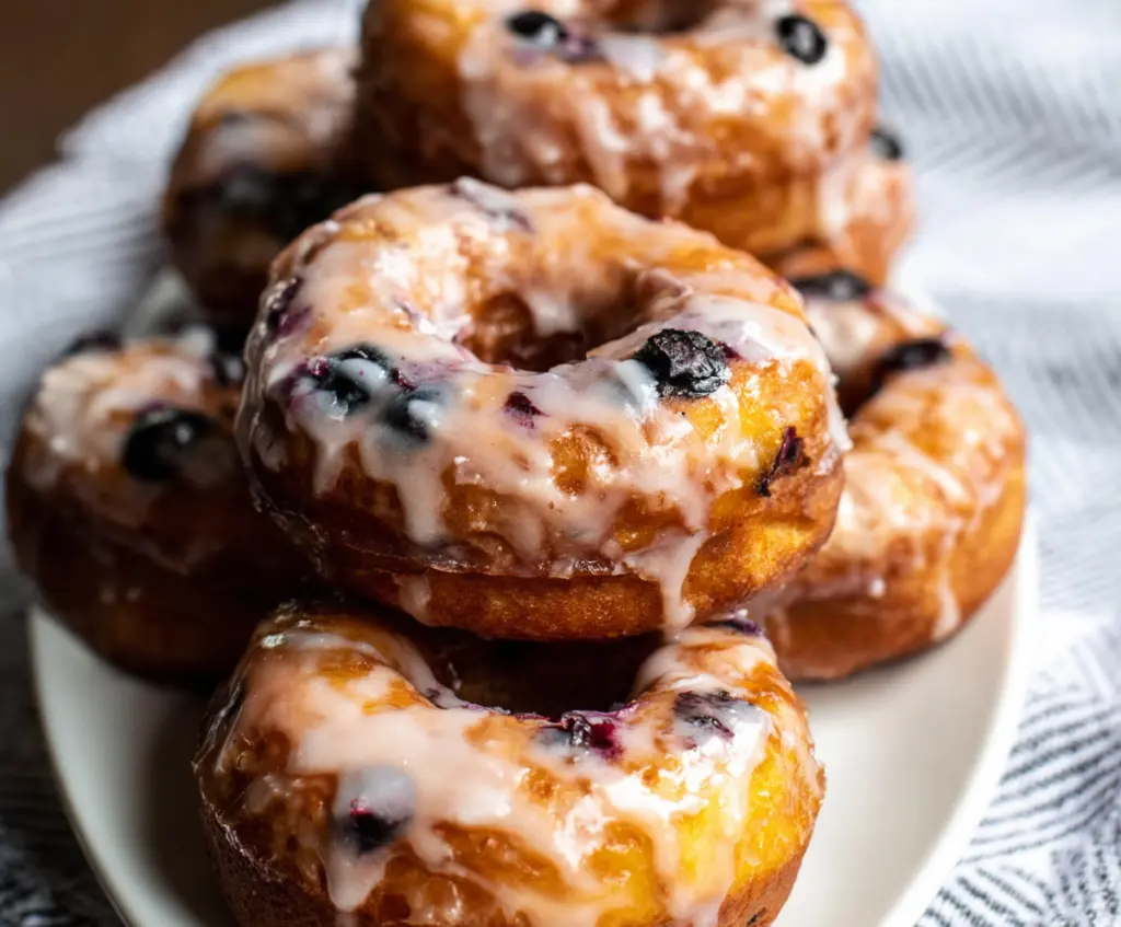 Delicious blueberry cake donuts with fresh blueberries topping a golden-brown donut on a white plate.