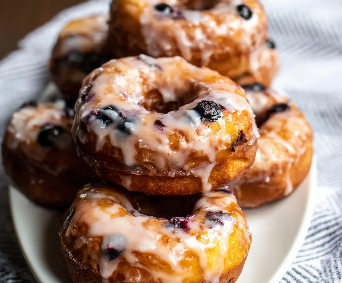 Delicious blueberry cake donuts with fresh blueberries topping a golden-brown donut on a white plate.