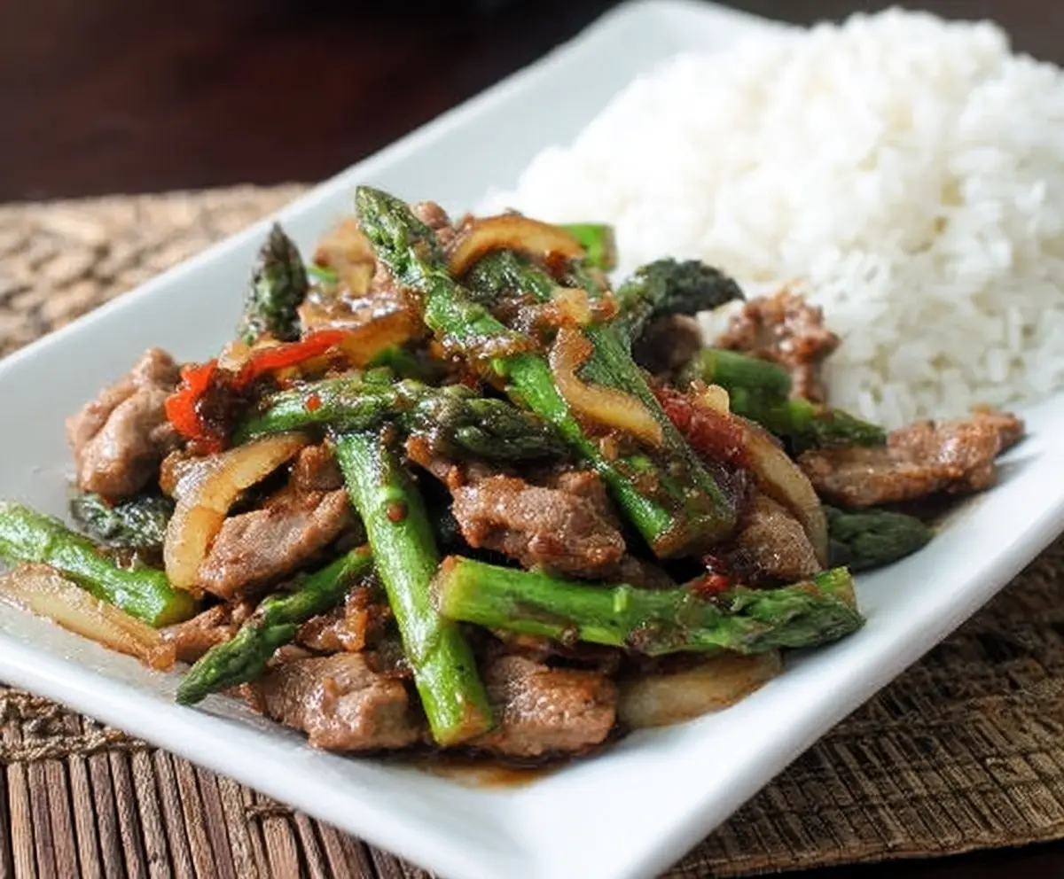 Delicious pork and asparagus stir fry served on a plate, garnished with sesame seeds.